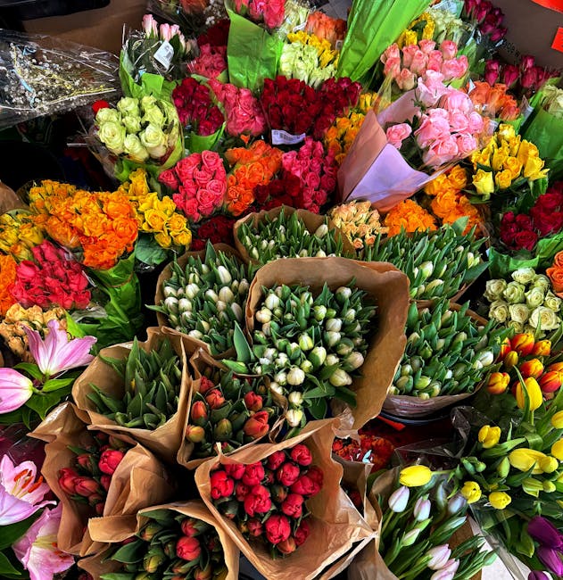 A vibrant display of freshly cut flowers arranged in bouquets, featuring a variety of colours including pink, red, yellow, orange, and white. The flowers consist of roses, tulips, and lilies, wrapped 